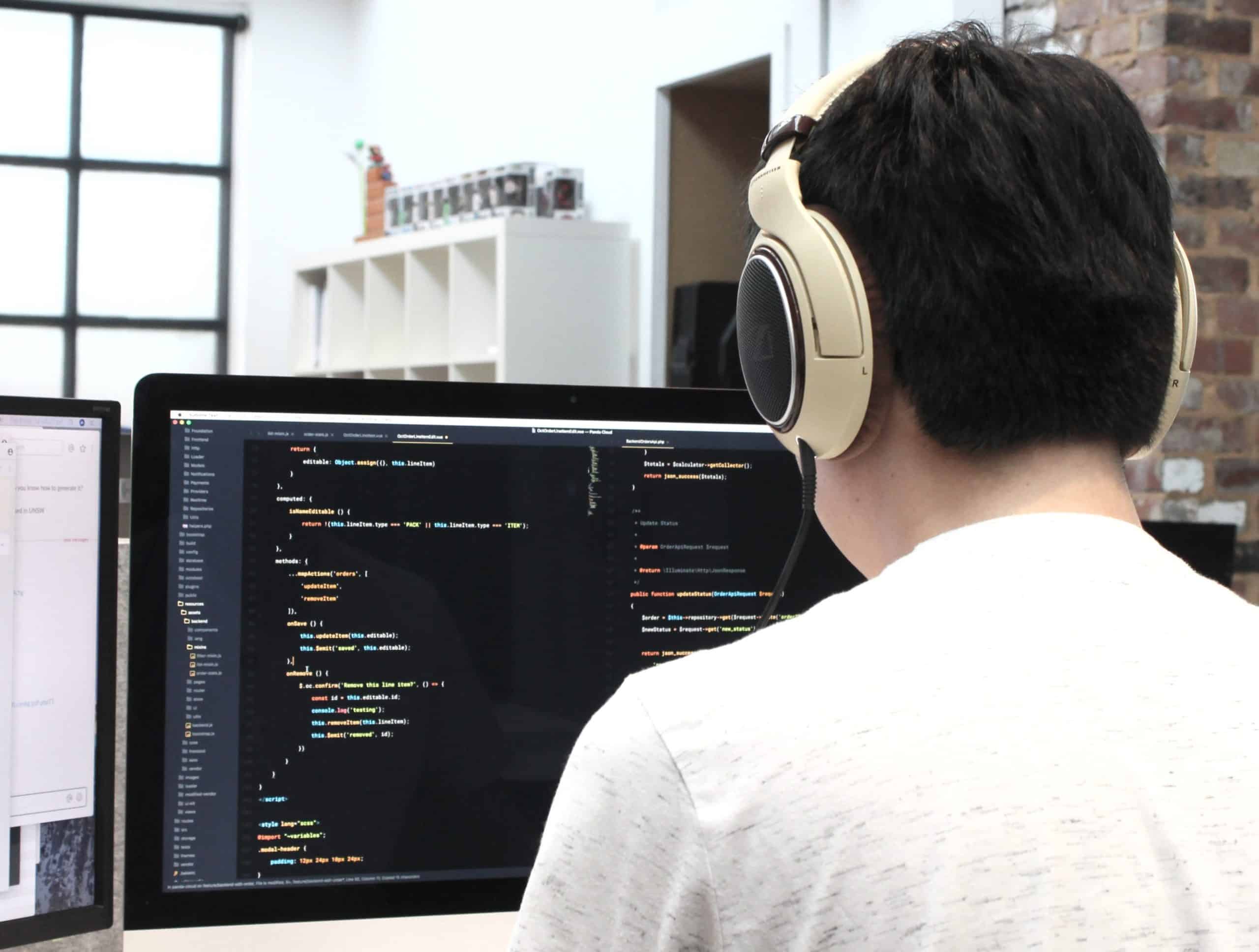 software developer with headphones coding on two screens